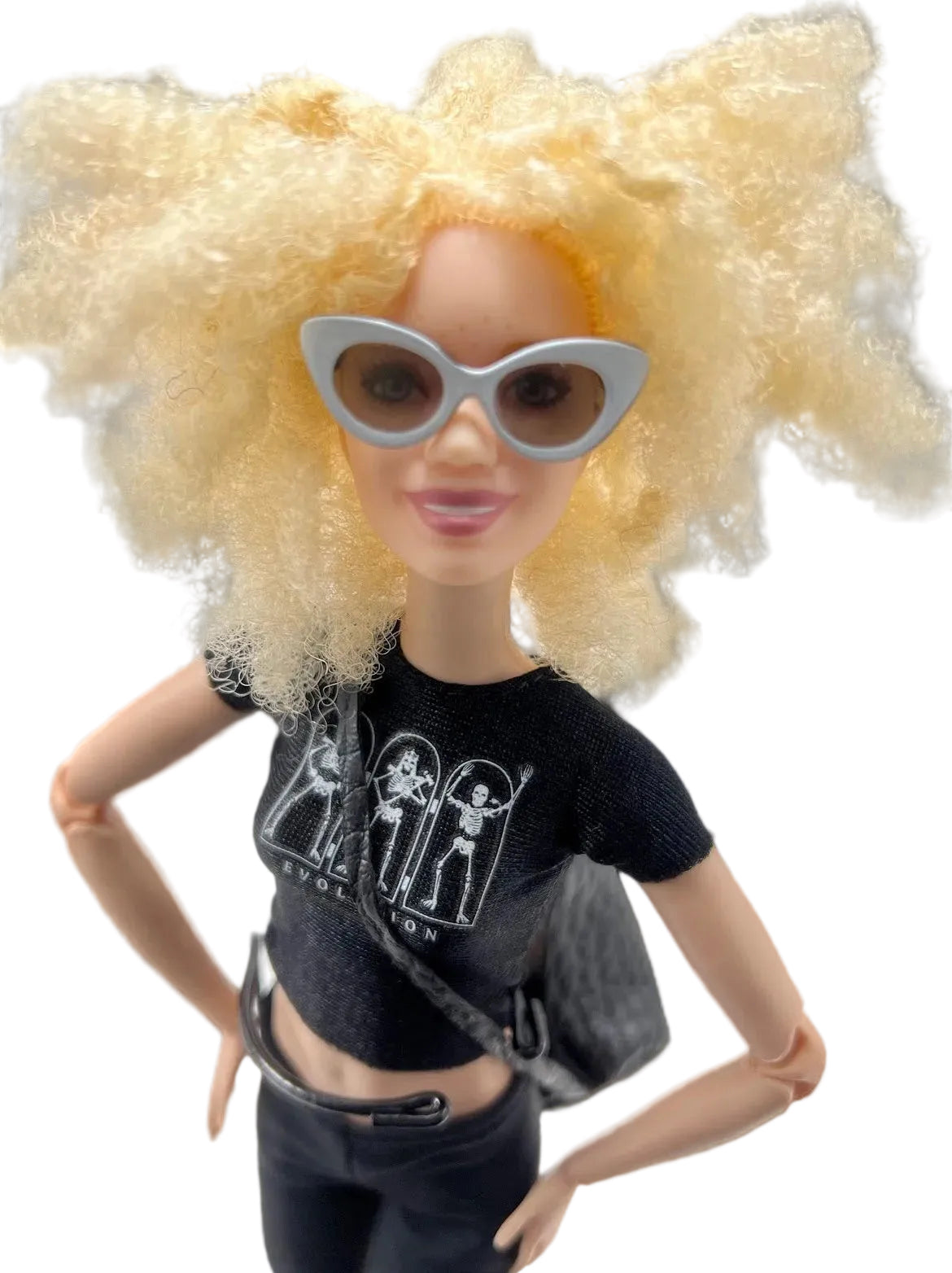 Doll with blonde hair, sunglasses, black t-shirt, and pants on a gray background