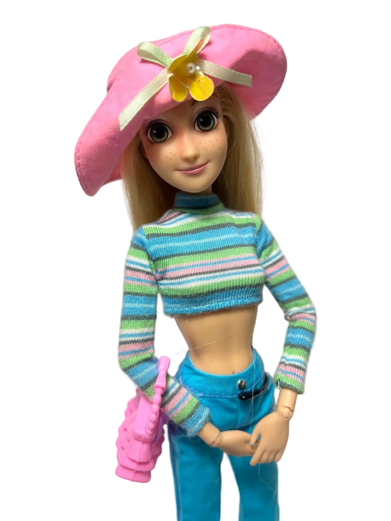 Doll wearing a colorful striped sweater and pink hat on a plain background
