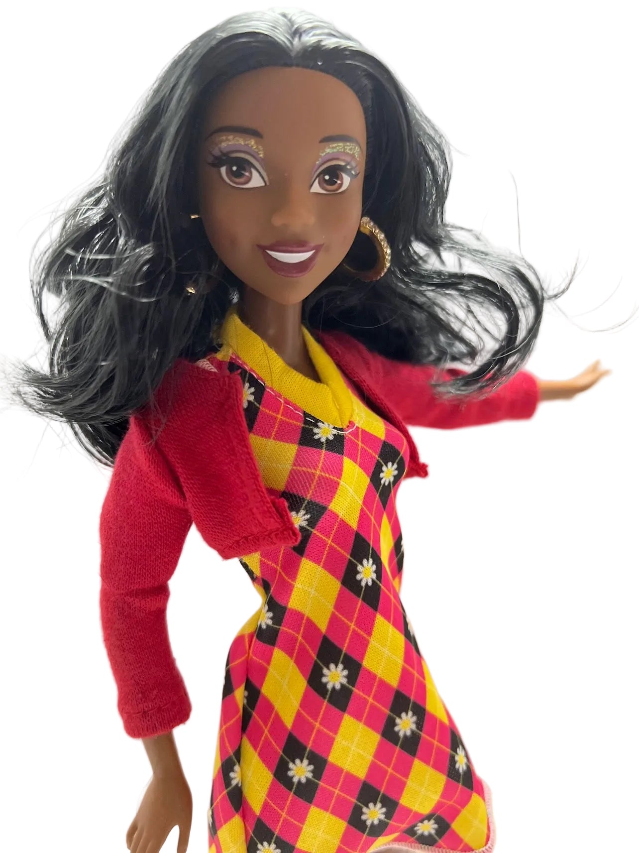 Doll wearing a red sweater and yellow checkered dress with floral patterns on a plain background